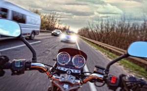 First-person view of a motorcyclist riding on the wrong side of the road about to crash into a car.
